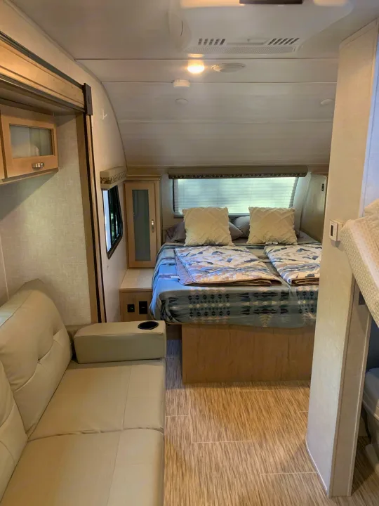 Cozy rv rental interior featuring a bed with patterned blankets, a small sofa with cup holder, and modern wood-look flooring.. R-Pod Hood River Edition 2020
