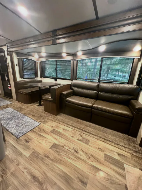 Experience comfort in this RV rental! Interior view of a living area with a large leather sofa, dinette, and bright window views.. Keystone Cougar Half-Ton 2021