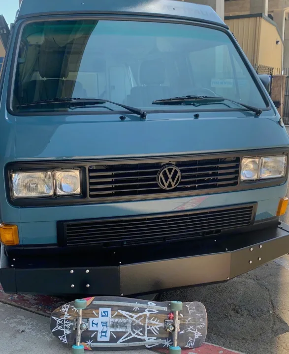 Front view of a blue VW Vanagon Westfalia, ideal for an rv rental road trip, with a skateboard resting on the ground.. Volkswagen Westfalia 1990