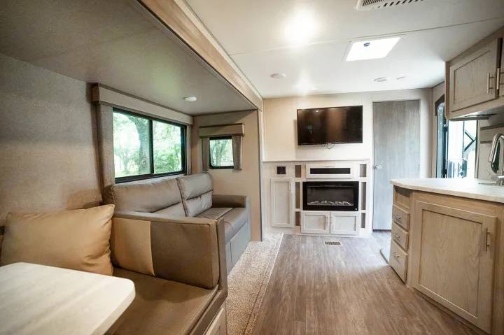 Spacious RV rental living area features a light gray sofa, large windows, entertainment center with TV & electric fireplace, and kitchen counter.. Forest River Coachmen Aurora 2022
