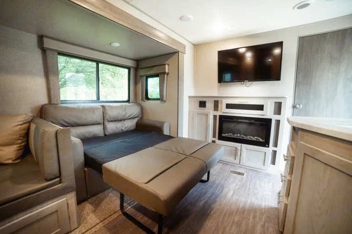 An inviting RV rental living area featuring a sofa bed, electric fireplace, TV, and large windows for scenic views.. Forest River Coachmen Aurora 2022