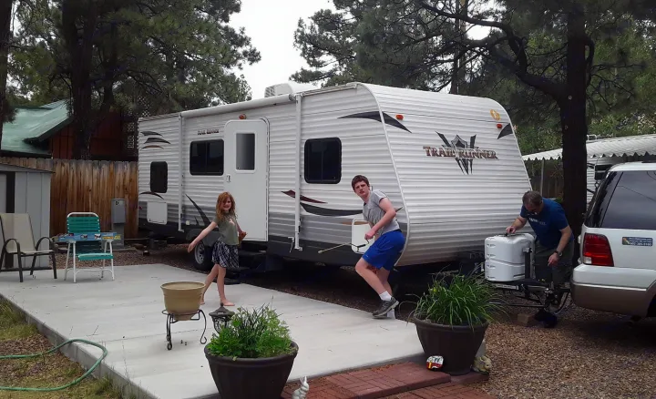 Family readies their RV rental. A man works on the travel trailer hitch, as two kids play nearby on a concrete patio.. Heartland RVs Trail Runner 2013