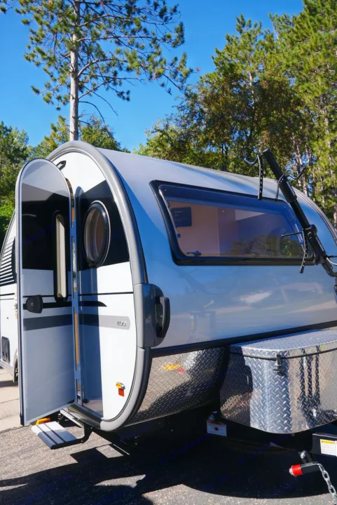 This silver and white teardrop RV rental with its door open is ready for your next outdoor camping adventure.. Nucamp Tab 400 2022