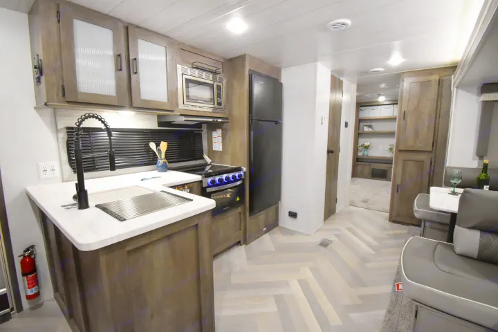 This modern RV rental features a compact kitchen with a sink, stove, microwave, fridge, and an adjacent dining area.. Forest River Salem 2020