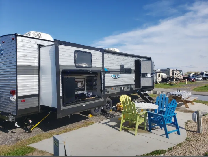 RV rental travel trailer set up at a sunny campsite with an outdoor entertainment area and patio seating.. Forest River Salem 2020