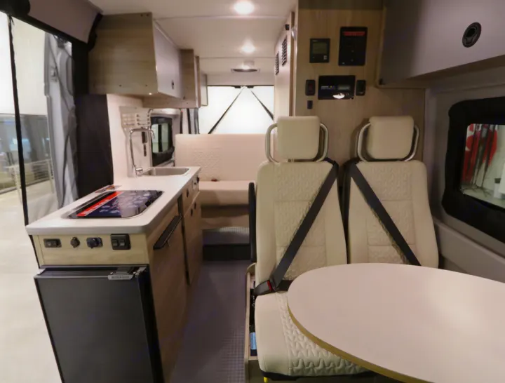Interior of a modern RV rental featuring a well-equipped kitchen, comfortable seating for passengers, dining table, and control panel.. Winnebago Solis 2022