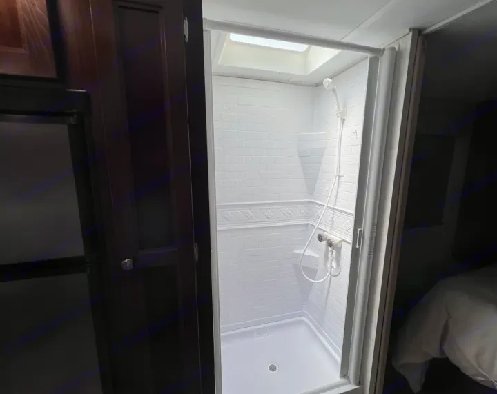 Well-lit RV rental shower with white textured walls and an overhead skylight, seen from outside the compact stall.. Forester LE 2020