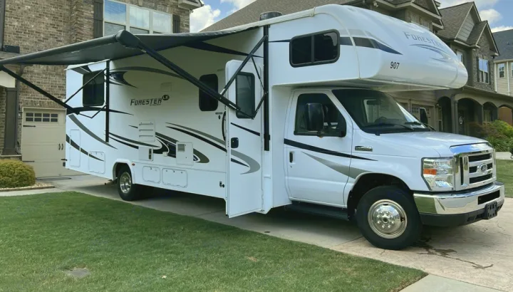 A clean white Forester motorhome RV rental parked in a residential driveway with its awning extended next to a brick house.. Forester LE 2020