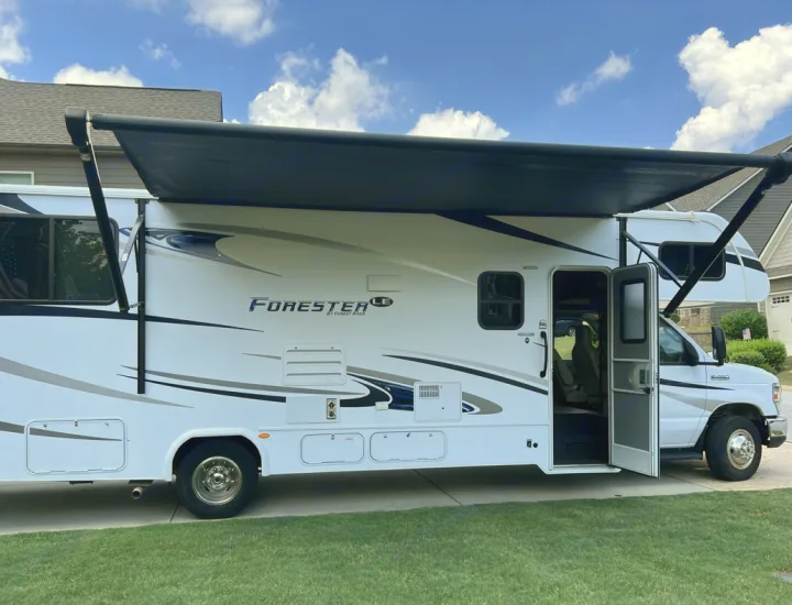 White Class C motorhome with an extended black awning and open door, perfect for an RV rental adventure.. Forester LE 2020