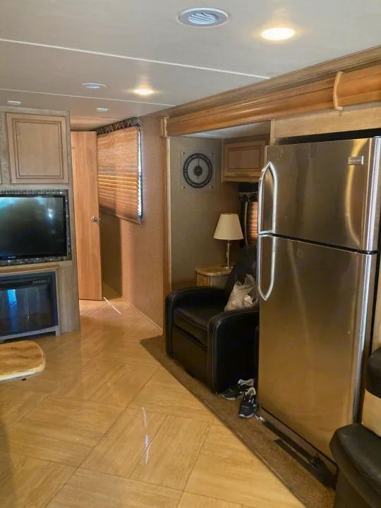 Inside an RV rental: a modern living area with a stainless steel fridge, TV, fireplace, and comfy black armchair.. 1F66F5DY4E0A13513 37SA 2015