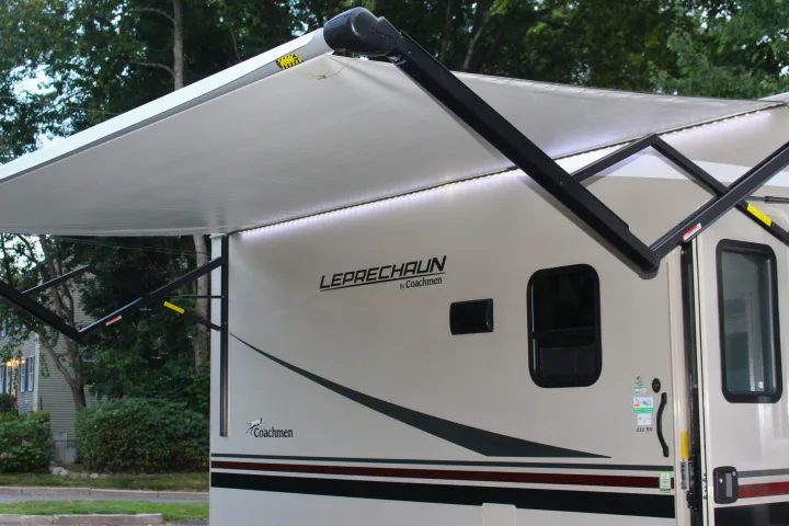 Side view of a Coachmen Leprechaun RV rental with its illuminated awning extended, perfect for outdoor leisure.. Forest River Coachmen Leprechaun 2022