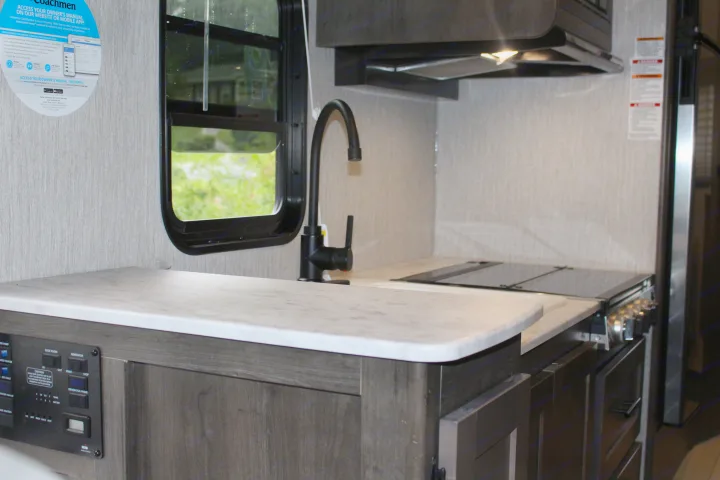 Functional RV rental kitchen with white marble-look counters, a black faucet, cooktop, and interior control panel.. Forest River Coachmen Leprechaun 2022