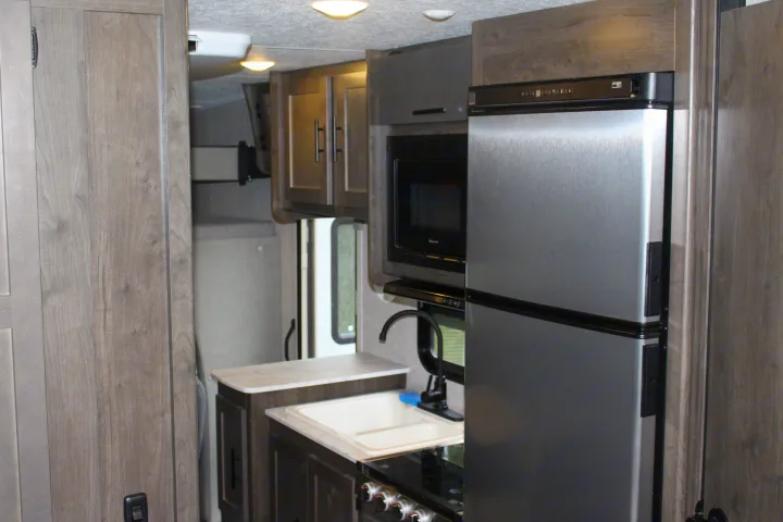 Inside a contemporary RV rental: a well-equipped kitchen featuring a fridge, microwave, sink, and stovetop.. Forest River Coachmen Leprechaun 2022