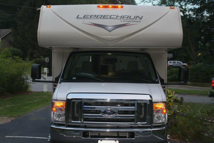 Front view of a white Coachmen Leprechaun RV rental, a Ford motorhome with bright lights on, ready for your travel.. Forest River Coachmen Leprechaun 2022