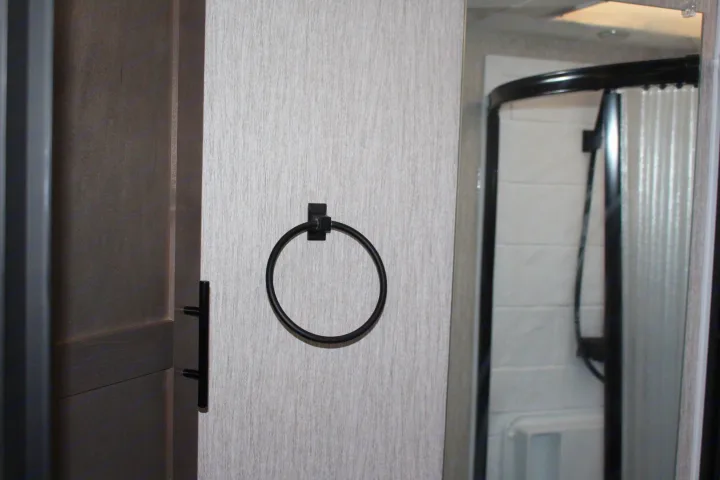 Modern RV rental bathroom featuring a black towel ring, dark door handle, and curved shower enclosure.. Forest River Coachmen Leprechaun 2022