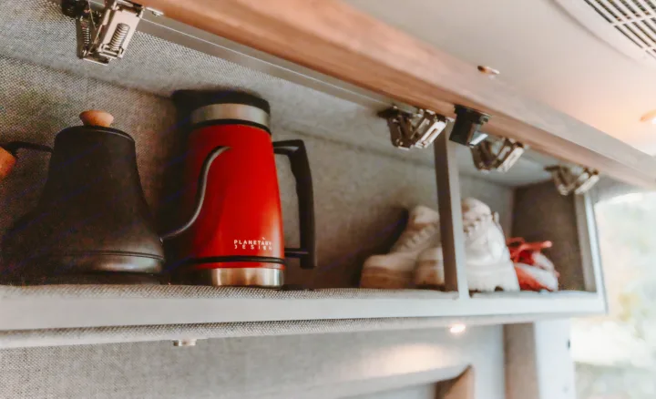 Inside an RV rental: neatly stored travel essentials including a black kettle and red pour-over coffee pot in overhead shelving.. StoryTeller Overland Classic Mode 4X4 2022