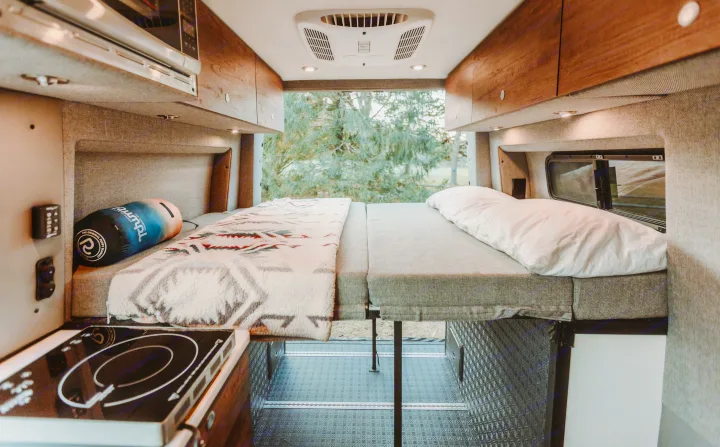 An RV rental's cozy interior, showing a modular bed, wood cabinets, and an induction cooktop. Ready for your adventure.. StoryTeller Overland Classic Mode 4X4 2022