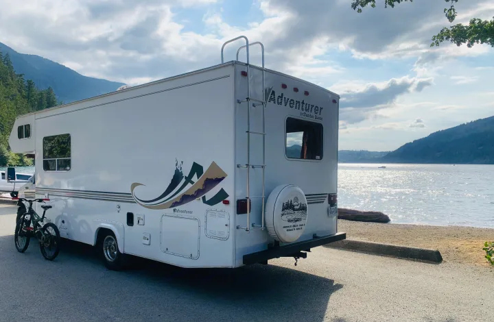 Adventurer RV rental parked lakeside with mountains, bicycles visible for adventure travel.. Slumber Queen Adventurer 2001