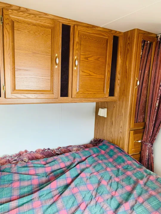 RV rental interior: overhead wood cabinets, cozy plaid bed, and patterned curtains in the sleeping area.. Slumber Queen Adventurer 2001
