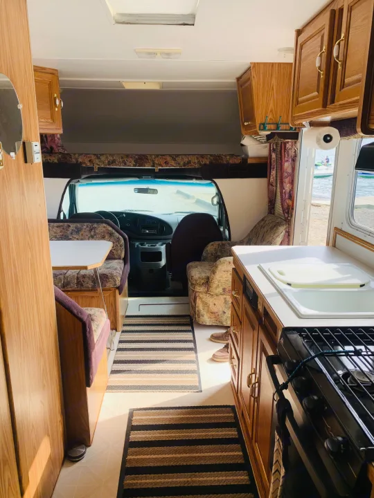 Spacious RV rental interior featuring a kitchen, dining area, and driver's cab, with a scenic lake view outside.. Slumber Queen Adventurer 2001