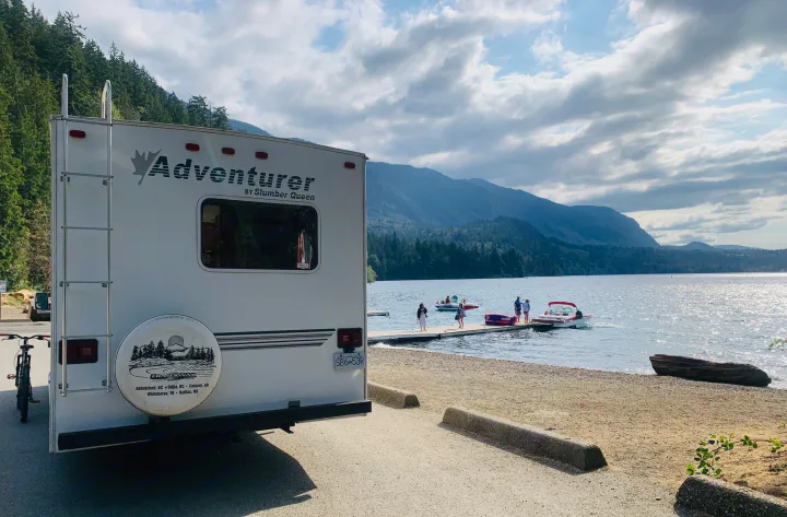 Adventurer RV rental parked by a scenic BC lake, with mountains, boats, and people on a dock.. Slumber Queen Adventurer 2001