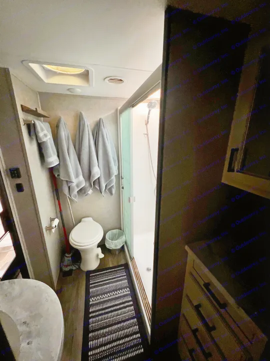 Compact RV rental bathroom featuring a toilet, shower, sink, and hanging towels.. Highland Ridge RV Open Range 2021