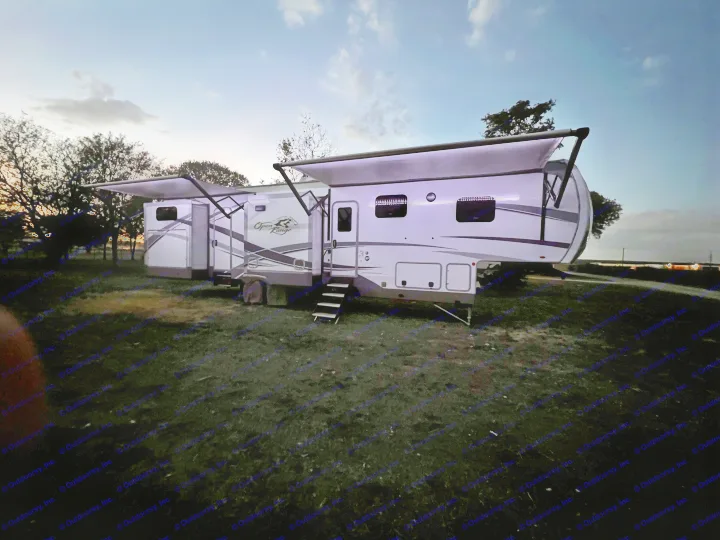 Large white RV rental, brightly lit with extended awnings, parked on a grassy field under a twilight sky.. Highland Ridge RV Open Range 2021