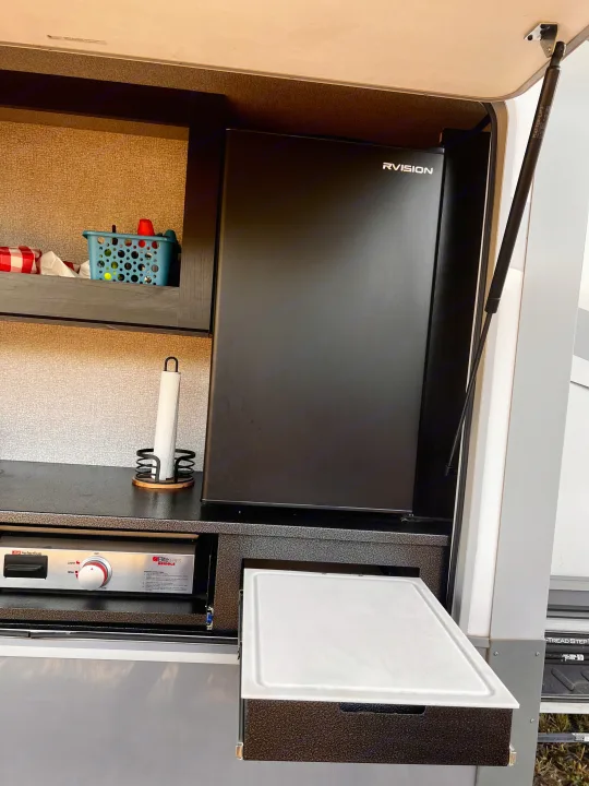 RV rental outdoor kitchen featuring a Suburban griddle, RVISION fridge, and pull-out prep board.. Highland Ridge RV Open Range 2021