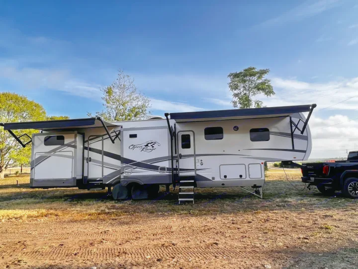 This Open Range fifth-wheel RV rental, hitched to a pickup truck, is set up in a sunny outdoor spot, ready for adventure.. Highland Ridge RV Open Range 2021