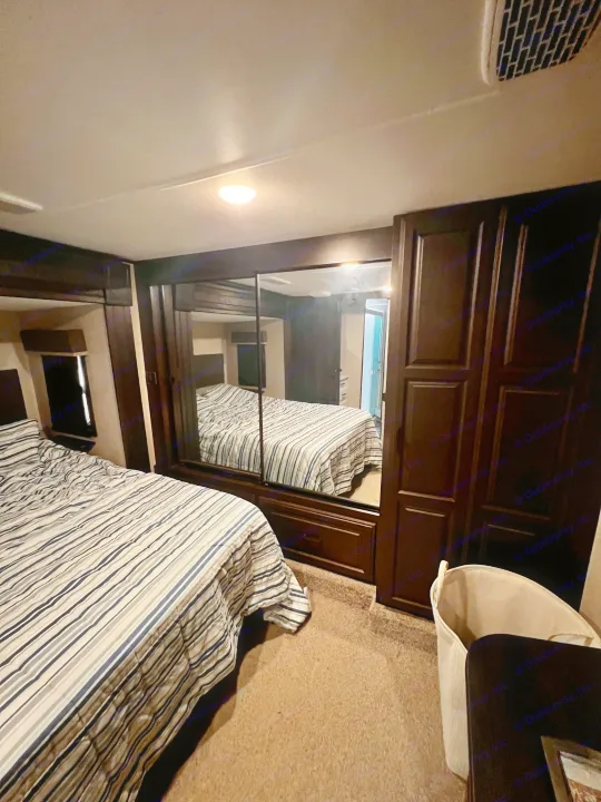 RV rental bedroom with a striped bed, large mirrored wardrobe, and ceiling vent, showing dark wood finishes.. Highland Ridge RV Open Range 2021