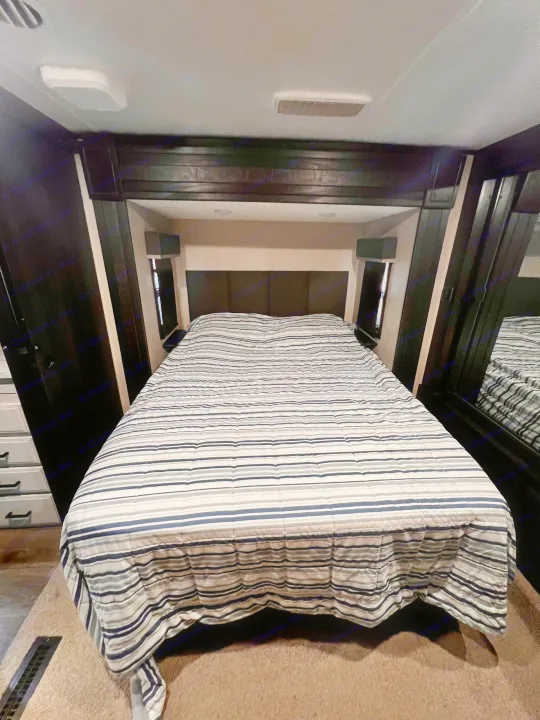 Comfortable RV rental bedroom with a striped comforter, built-in storage, and mirror. Perfect for travel!. Highland Ridge RV Open Range 2021