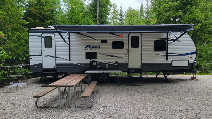This RV rental, a travel trailer, is parked on a gravel campsite with an extended awning and picnic table.. Forest River Puma 2017