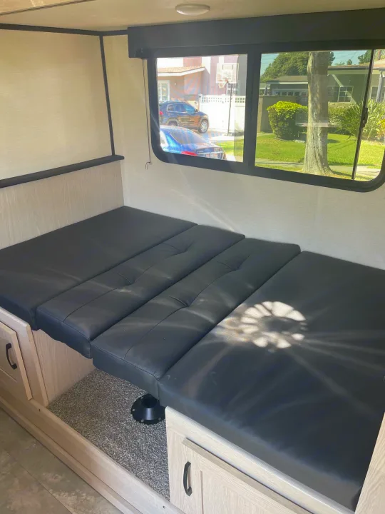 Inside this RV rental: a black cushioned dinette converts to a bed, with light wood storage and large windows.. Forest River Coachman Apex Nano 2022