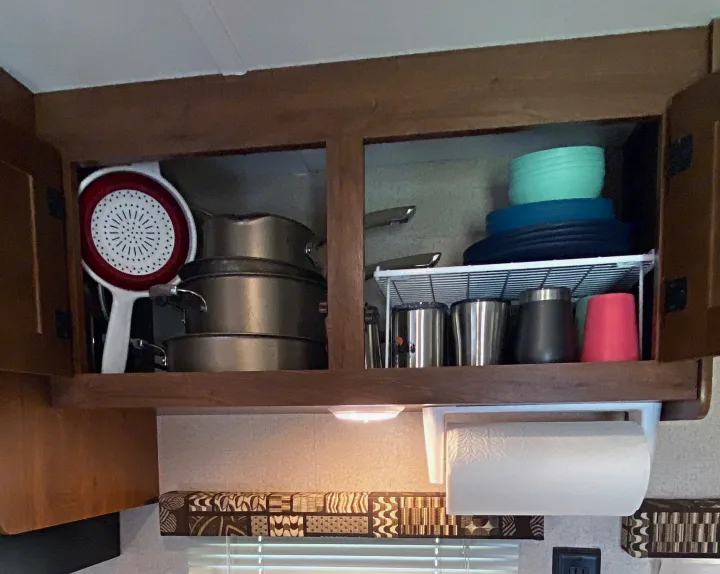 RV rental kitchen cabinet open, displaying stacked pots, colorful bowls, travel mugs, and a colander. Compact organization.. Jayco Jay Flight SLX 2016