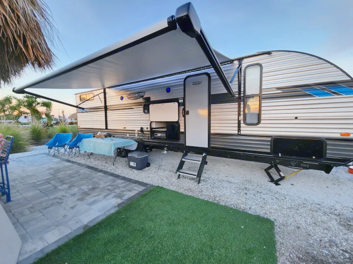 Spacious RV rental, ready for outdoor fun. Features an extended awning, outdoor kitchen, table, and chairs at a relaxing campsite.. Forest River Salem Cruise Lite 2022