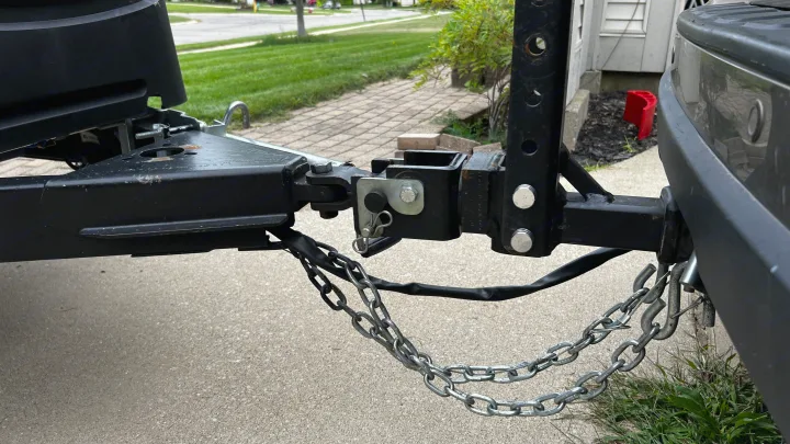 A close-up view of an RV rental's trailer hitch, coupler, and safety chains securely connected to a towing vehicle.. TAXA Cricket Overland Edition 2020