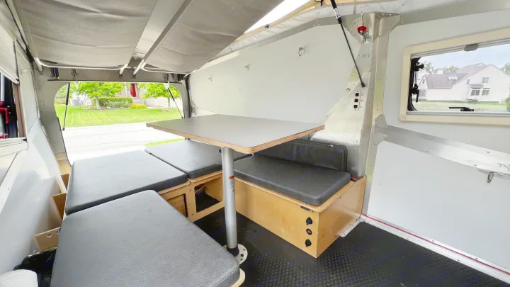 Inside a compact rv rental: a cozy dinette with dark cushions and a table, convertible to a sleeping area for comfortable travel.. TAXA Cricket Overland Edition 2020