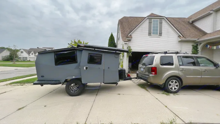RV rental: A sleek grey camper trailer, hitched to an SUV in a driveway, ready for outdoor adventure.. TAXA Cricket Overland Edition 2020