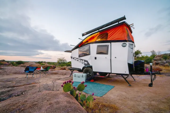 Experience outdoor adventure with an RV rental! A "Cricket" travel trailer set up for camping on a rocky landscape at dusk.. TAXA Cricket Overland Edition 2020