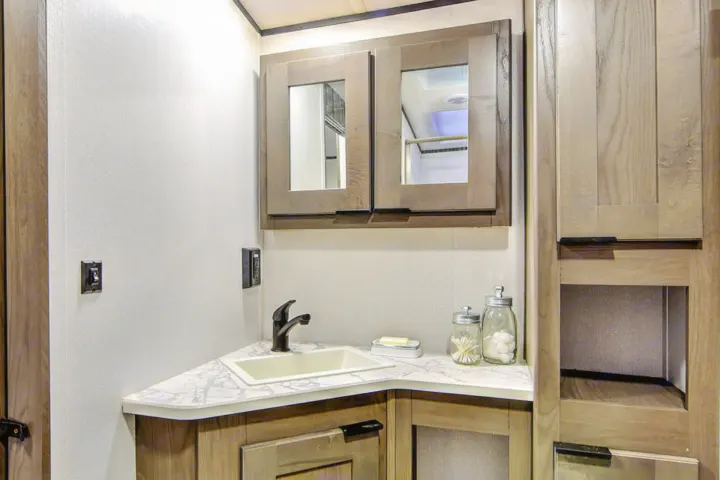 Compact RV rental bathroom with corner sink, sleek faucet, mirrored cabinet, and wood storage. Clean, functional space.. Cruiser RV MPG Ultra Lite 2022