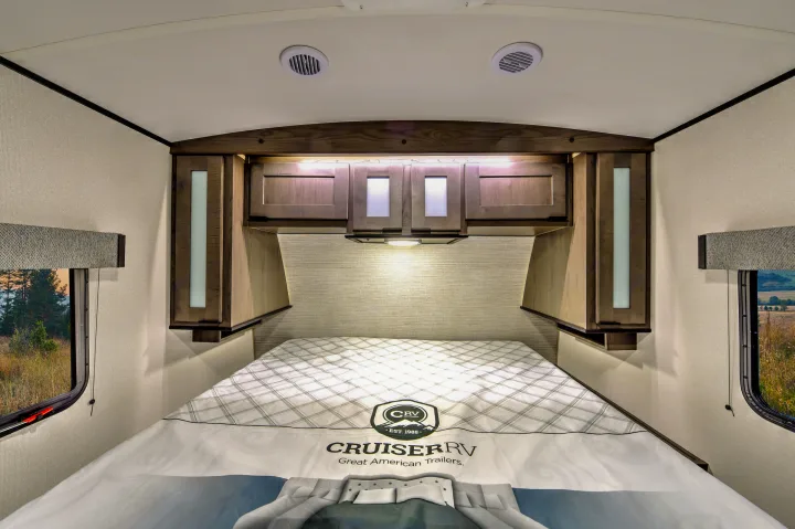 Cozy RV rental bedroom with overhead storage, soft lighting, and window views for a comfortable journey.. Cruiser RV MPG Ultra Lite 2022