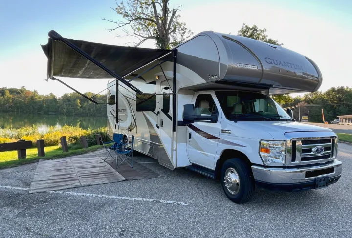Quantum Class C RV rental by a tranquil lake with awning extended and chairs set. Perfect for a scenic outdoor escape.. Thor Quantum 2017