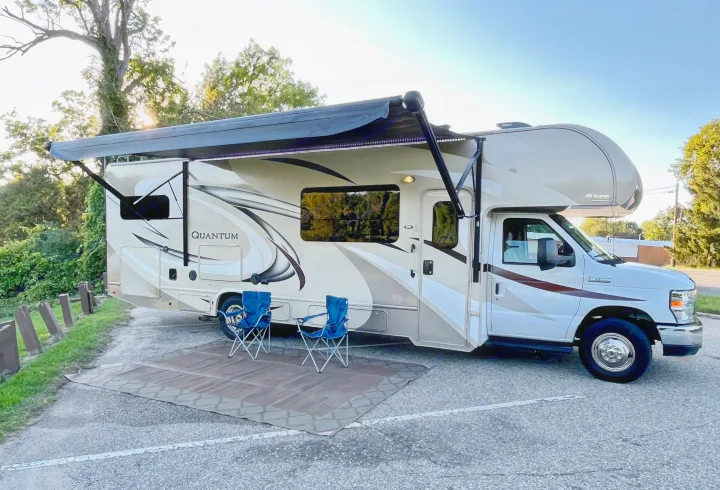 RV rental: A Thor Quantum motorhome with extended awning and LED lights, blue chairs, and a mat set up for camping.. Thor Quantum 2017