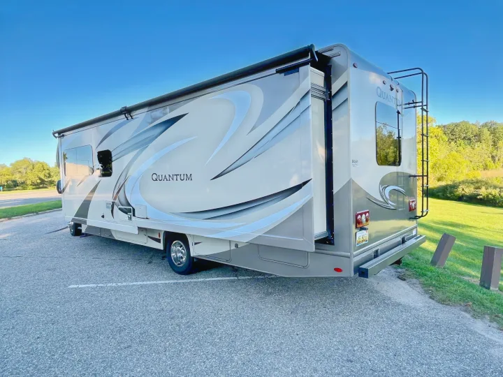 This spacious Quantum RV rental, light-colored with grey graphics, is parked on asphalt with its slide-out extended.. Thor Quantum 2017