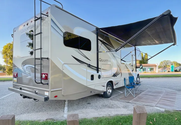 Spacious Quantum RV rental with extended awning, two blue chairs, and ground mat set up for a relaxing outdoor stop.. Thor Quantum 2017