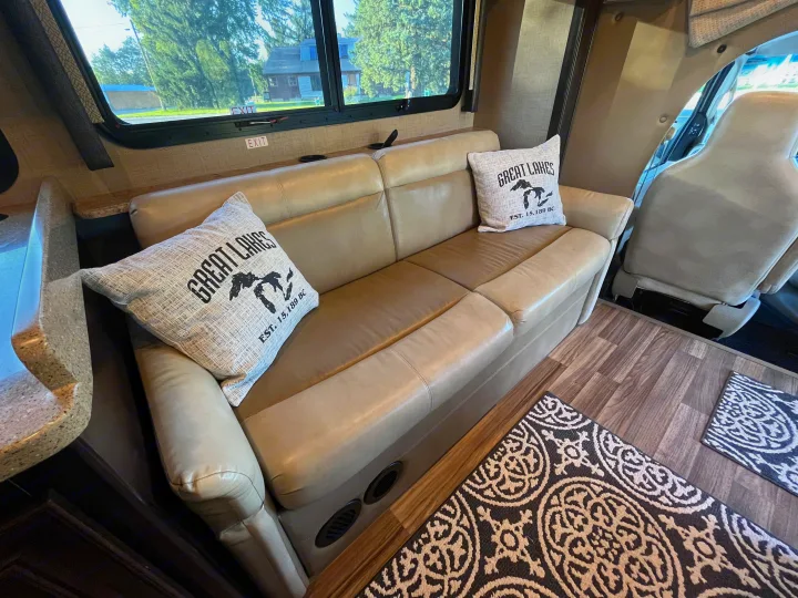 RV rental interior featuring a comfy sofa with Great Lakes pillows, hardwood floors, and a view of trees outside.. Thor Quantum 2017