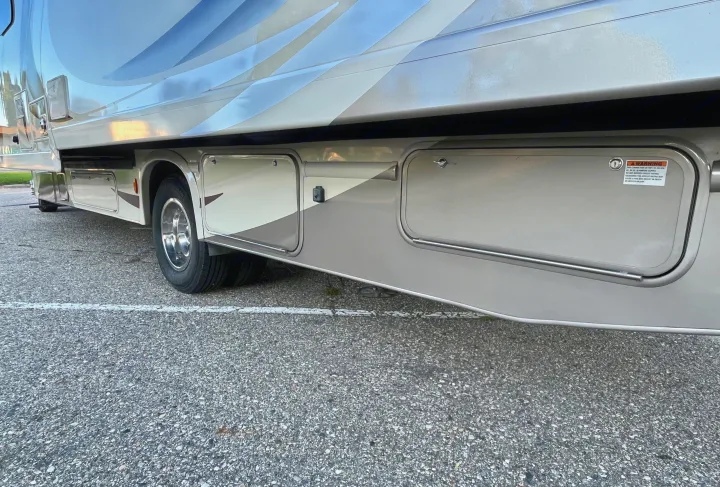 Side view of an RV rental, highlighting external storage compartments and a visible warning label on an access door.. Thor Quantum 2017