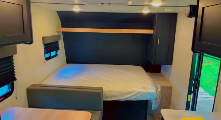 This RV rental interior features a cozy mattress, dark accent wall with wood trim, storage cabinet, and bright windows.. Keystone RV Springdale 2022