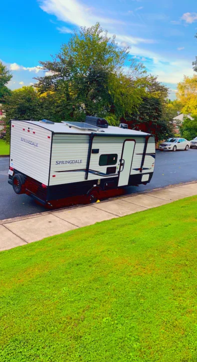 A white Springdale RV rental, equipped with solar panels, is parked curbside on a sunny day near green grass.. Keystone RV Springdale 2022