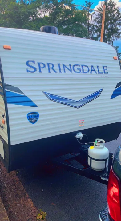 Explore with this Springdale by Keystone travel trailer, available for RV rental. White with blue graphics, visible propane tank.. Keystone RV Springdale 2022